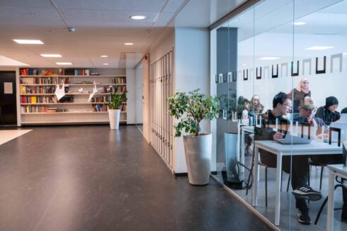 Korridor i skolan med glasvägg in till ett klassrum där elever jobbar på sina datorer